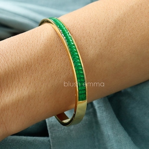May include: A gold bangle bracelet with a green enamel band. The band is made up of small, square-shaped pieces of enamel.