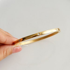 May include: A gold bangle bracelet with small clear stones set into the band.