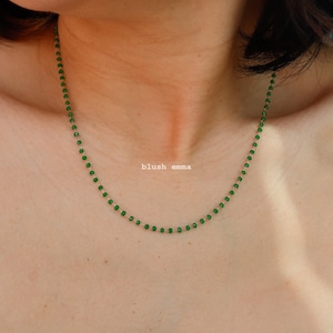 May include: A delicate gold chain necklace with small green beads. The necklace is worn by a person, but the focus is on the necklace itself.