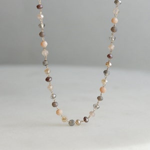 May include: A delicate gold chain necklace with small, multi-colored beads in shades of pink, brown, and gray.