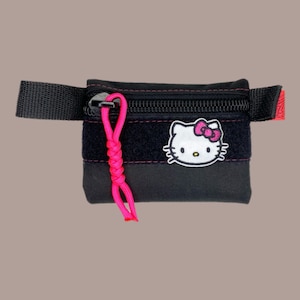 May include: A black zippered pouch with a Hello Kitty patch and a pink cord. The pouch has a black strap and a zipper closure.
