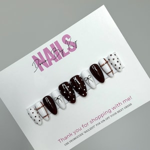May include: A collection of false nails featuring designs such as white with black polka dots, bows, and copper-coloured lines, alongside dark burgundy with white polka dots. The text "NAILS Done By Ky" is visible.