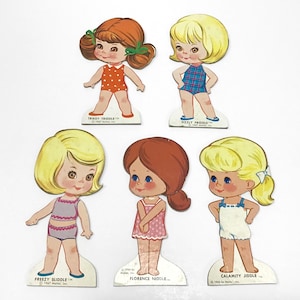 May include: A collection of vintage paper dolls featuring six different girls. Each doll is dressed in a swimsuit or romper and has a unique hairstyle. The dolls are printed on cardboard and have the names "Trikey Triddle", "Sizzly Friddle", "Calamity Jiddle", "Freezy Sliddle", and "Florence Niddle".