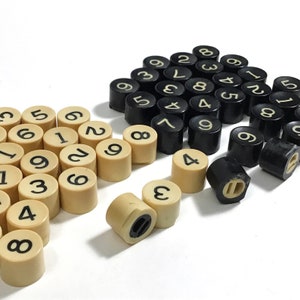 May include: A collection of black and cream plastic number tiles. The tiles are arranged in two groups, one group of black tiles and one group of cream tiles. The tiles are numbered 1 through 9.