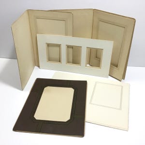 May include: A collection of vintage photo mats and frames in various sizes and styles. The frames are in shades of brown, cream, and off-white. Some have decorative borders, while others have multiple openings for displaying photos. The items are arranged on a white surface.