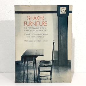 May include: A book cover titled "SHAKER FURNITURE" with text about the craftsmanship of an American communal sect. The cover features a black and white image of a table, chair, and grandfather clock. The book is by Edward Deming Andrews and Faith Andrews.
