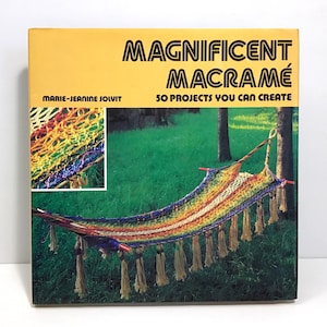 May include: A book cover with the title "Magnificent Macramé" and the subtitle "50 Projects You Can Create." The cover features a colorful macramé hammock with tassels, set against a backdrop of green grass and trees. A smaller inset shows a close-up of macramé.