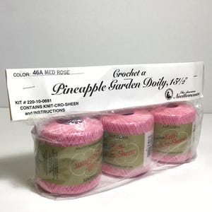 May include: A package of three spools of pink crochet thread, labeled "Knit-Cro-Sheen," for a Pineapple Garden Doily. The package includes instructions and is color 46A Med Rose. The doily is 15.5 inches in diameter.
