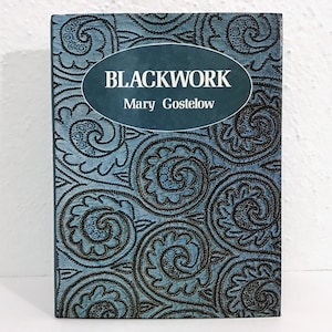 May include: A book titled "BLACKWORK" by Mary Gostelow. The book cover has a teal background with a repeating black floral pattern. The title and author's name are in white text inside a teal oval.