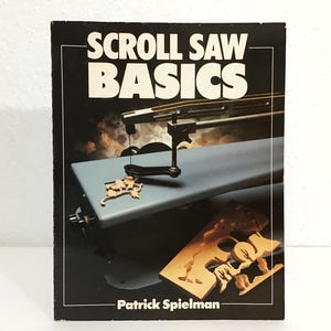 May include: A book cover titled "SCROLL SAW BASICS" with a black border. The cover features a scroll saw and wooden cutouts. The author's name, Patrick Spielman, is at the bottom. The background has a smoky, orange and brown effect.