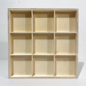 May include: A square wooden display shelf featuring nine equal-sized compartments arranged in a three-by-three grid. The organizer is constructed from light-colored plywood with visible grain, showcasing a clean, open-front design for storage.
