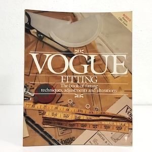 May include: A vintage Vogue Fitting book with the text "VOGUE FITTING" in large white letters. The book cover features sewing tools, including scissors and a measuring tape. The book's subtitle reads "The book of fitting techniques, adjustments and alterations."