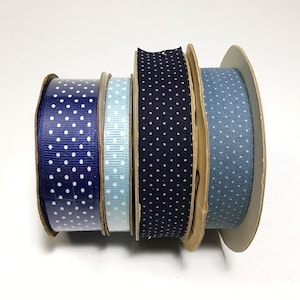 May include: A collection of spools of ribbon in various shades of blue, each adorned with white polka dots. The ribbons are arranged side by side, showcasing a range of textures and patterns, perfect for crafting and gift wrapping.