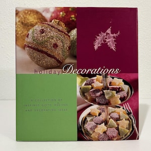 May include: A square book cover titled holiday Decorations featuring a collection of inspired gifts, recipes, and decorating ideas. The cover displays a glittery gold ornament, a dark red section with white holly, and a two-tiered silver tray of star-shaped candies.