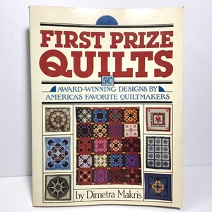 May include: A vintage book titled "FIRST PRIZE QUILTS" with red and black lettering. The cover features various quilt designs in a grid, showcasing award-winning designs by American quiltmakers. The author's name, Dimetra Makris, is also displayed.