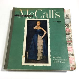 May include: A December 1952 issue of McCall's magazine with a green cover featuring a central photograph of a person in a blue and white ruffled gown. The right edge has white index tabs listing clothing categories like dresses, suits, and coats.
