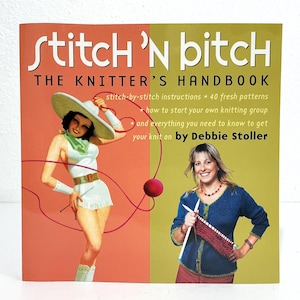 May include: A softcover book titled Stitch 'n Bitch: The Knitter's Handbook by Debbie Stoller. The cover features a split orange and green background with an illustration of a person in a white outfit and a photo of a person knitting with needles.