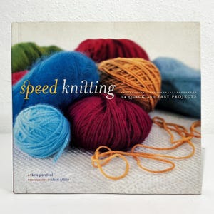 May include: A square book titled Speed Knitting: 24 Quick and Easy Projects by Kris Percival with photographs by Sheri Giblin. The cover features a collection of colorful yarn balls in shades of blue, red, orange, and green on a white surface.