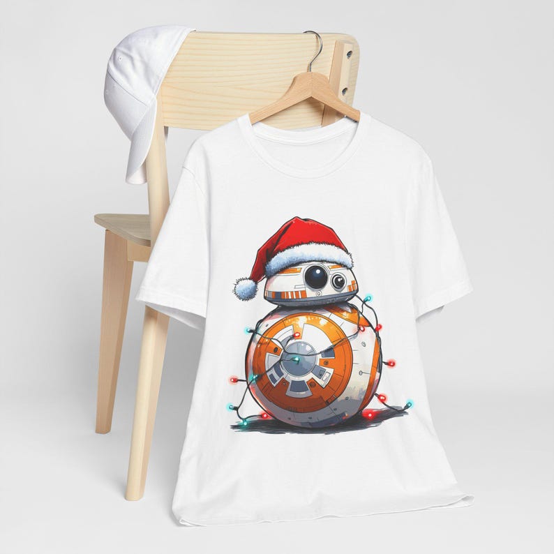 Peut inclure: T-shirt blanc avec une image de dessin anim&eacute; d'un dro&iuml;de portant un chapeau de P&egrave;re No&euml;l et envelopp&eacute; de lumi&egrave;res de No&euml;l.