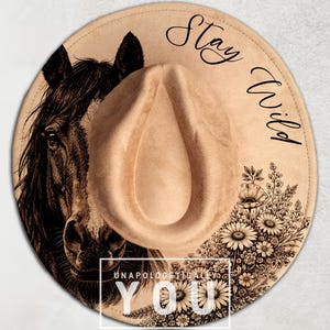 May include: A tan cowboy hat with a horse illustration and floral design. The hat features the words "Stay Wild" and "Unapologetically You". The hat is a stylish accessory.