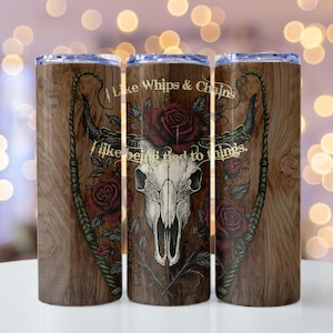May include: Three stainless steel tumblers with a wooden texture background. Each tumbler features a design with a skull, roses, and the text "I like whips & chains, I like being tied to things."