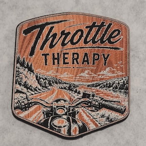 May include: A shield-shaped wooden plaque featuring a black graphic print of a motorcycle handlebar view overlooking a winding road through a forest. The text "Throttle THERAPY" is printed in black at the top against the natural wood grain background.