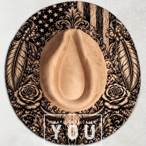 May include: A tan felt hat with a wide brim featuring a black graphic print of an American flag, roses, feathers, and a bull skull. The text UNAPOLOGETICALLY YOU is printed in white capital letters inside a rectangular frame at the bottom.