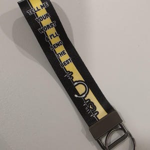 May include: Black and yellow keychain wrist strap with the text "TELL ME YOUR WORST & I'LL SEND THE BEST". The strap features a stethoscope and heartbeat graphic, and a metal key ring.
