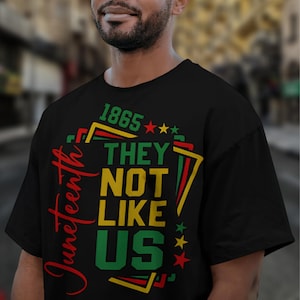 May include: Black t-shirt with a graphic design celebrating Juneteenth. The design includes the text "Juneteenth" in red script, along with the words "THEY NOT LIKE US" in green and yellow, and the year "1865".