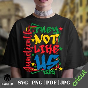 May include: Black t-shirt with a colorful graphic design. The design features the words "Juneteenth" and "THEY NOT LIKE US 1865" in green, yellow, red, and blue, with star accents. The shirt is layered and available in SVG, PNG, PDF, and JPG formats.