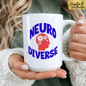 Peut inclure: Une tasse en céramique blanche avec un motif bleu et rouge. La tasse présente le texte "NEURO DIVERSE" en lettres bleues avec un graphique de cerveau rouge avec des engrenages bleus à l'intérieur.