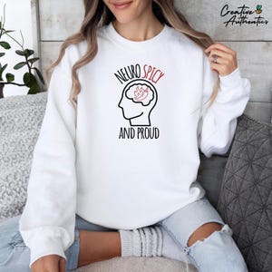 Könnte beinhalten: Weißer Pullover mit schwarzem Text, der "Neuro Spicy" lautet und einem Gehirn mit einer roten Chilischote darin. Der Text "And Proud" befindet sich unter dem Gehirn.