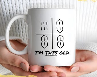 May include: White ceramic mug with a black and white meme graphic that says "I'm this old" and features a grid with four squares. The top left square has three vertical lines, the top right square has a backwards 'S', the bottom left square has a forward 'S', and the bottom right square has a forward 'S'.