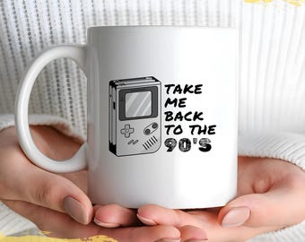 May include: White ceramic mug with a black and white illustration of a handheld video game console and the text "TAKE ME BACK TO THE 90'S".