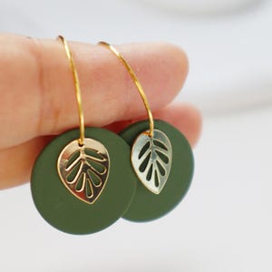Op de afbeelding: Een paar groene en gouden oorbellen met een bladerenontwerp. De oorbellen zijn gemaakt van polymer clay en hebben een gouden draadlus.