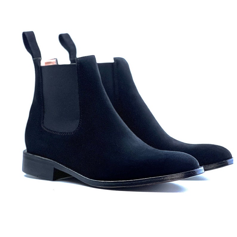 Peut inclure: Une paire de bottines Chelsea noires avec une finition mate lisse, des panneaux lat&eacute;raux &eacute;lastiques et deux languettes en haut de la cheville. Les bottines pr&eacute;sentent un petit talon et un bout arrondi, pr&eacute;sent&eacute;es sur un fond blanc uni.