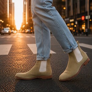Op de afbeelding: Lichtbruine su&egrave;de Chelsea boots met elastische zijpanelen en een lage hak, gedragen met een lichtblauwe spijkerbroek. De laarzen hebben een ronde neus, een treklipje bij de hiel en een bruine zool, in een klassiek instapmodel voor enkellaarzen.