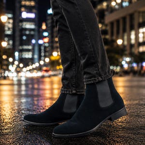 Peut inclure: Une paire de bottines Chelsea en daim noir avec des panneaux lat&eacute;raux &eacute;lastiques et un petit talon, port&eacute;es avec un jean en denim gris fonc&eacute;. Les bottines pr&eacute;sentent un bout arrondi et une languette &agrave; l'arri&egrave;re, offrant une forme &eacute;pur&eacute;e.