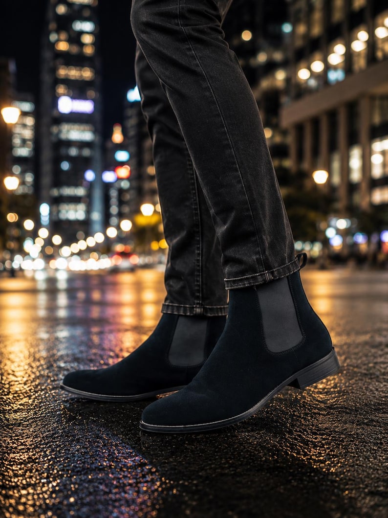 Peut inclure: Une paire de bottines Chelsea en daim noir avec des panneaux lat&eacute;raux &eacute;lastiques et un petit talon, port&eacute;es avec un jean en denim gris fonc&eacute;. Les bottines pr&eacute;sentent un bout arrondi et une languette &agrave; l'arri&egrave;re, offrant une forme &eacute;pur&eacute;e.