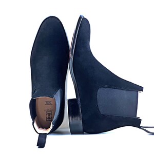 Peut inclure: Une paire de bottines Chelsea en daim noir avec des panneaux lat&eacute;raux &eacute;lastiques, un bout arrondi et un petit talon empil&eacute;. La semelle int&eacute;rieure affiche le nom de marque Grandeur avec un logo et du texte. Une tirette est fix&eacute;e &agrave; l'arri&egrave;re.