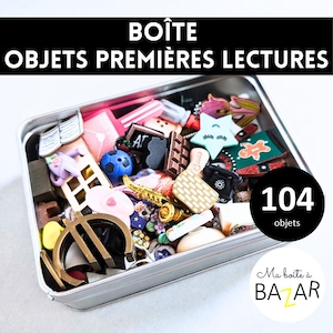 Op de afbeelding: Een metalen doos gevuld met diverse kleine objecten, waaronder een voetbal, een saxofoon en een chocoladereep. De doos heeft de tekst "BOÎTE OBJETS PREMIÈRES LECTURES" en "104 objets".