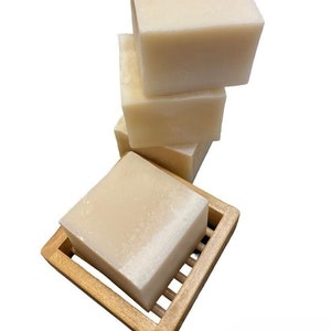 May include: Four bars of white soap stacked on top of each other, sitting on a wooden soap dish.