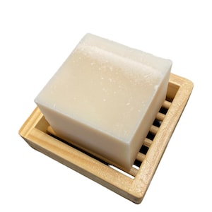 May include: A white bar of soap resting on a wooden soap dish with a slatted design.