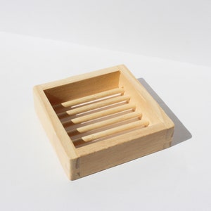 Könnte beinhalten: Eine Seifenablage aus Holz mit einem Lamellendesign. Die Ablage ist aus hellbraunem Holz und hat eine rechteckige Form.