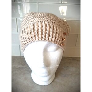 Puede incluir: Un gorro de punto beige con tres botones decorativos en el lateral.