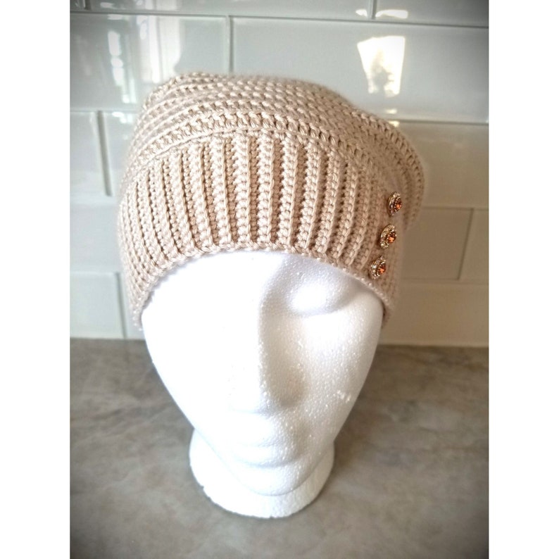 Puede incluir: Un gorro de punto beige con tres botones decorativos en el lateral.
