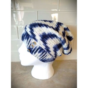 Puede incluir: Un gorro de punto azul y blanco con un ajuste holgado. El gorro tiene un patr&oacute;n texturizado y presenta tres botones plateados en el lateral.