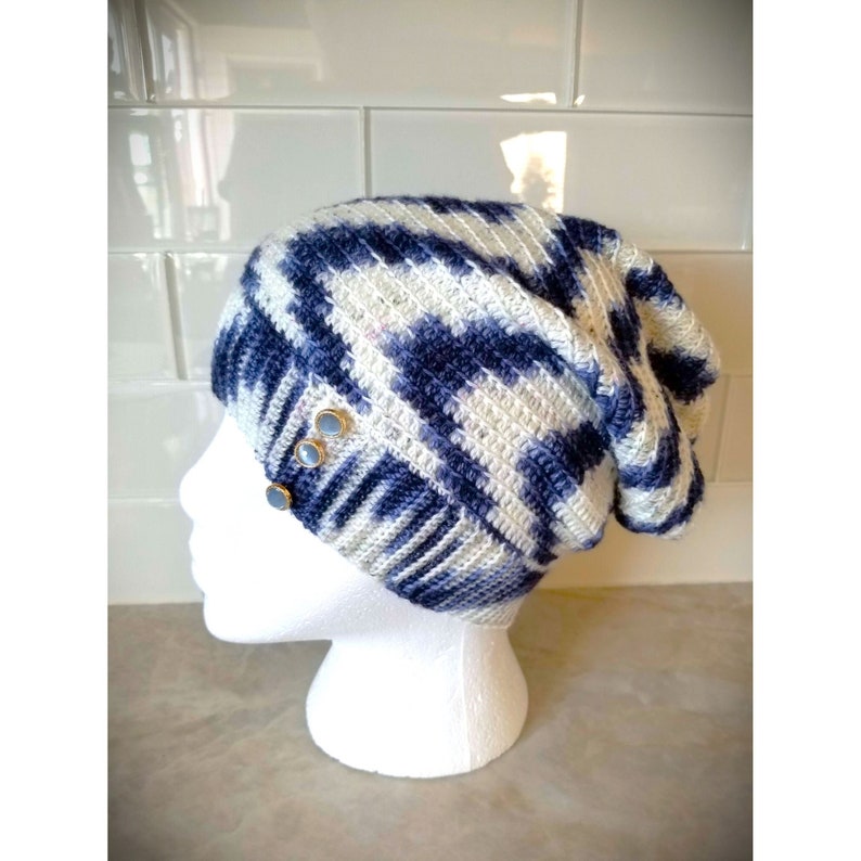 Puede incluir: Un gorro de punto azul y blanco con un ajuste holgado. El gorro tiene un patr&oacute;n texturizado y presenta tres botones plateados en el lateral.