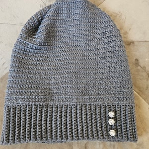 Puede incluir: Gorro de punto gris con tres botones de strass blancos en el lateral.