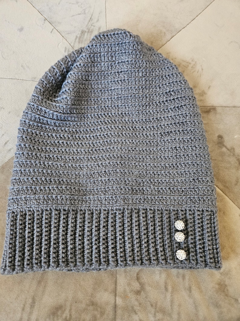 Puede incluir: Gorro de punto gris con tres botones de strass blancos en el lateral.